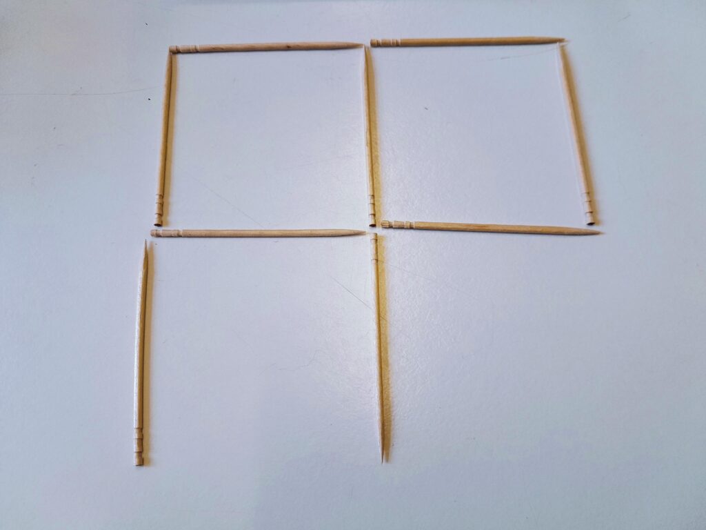 Photo of toothpicks on a table, making two adjacent squares, with toothpicks vertically down from the bottom corners of the left-hand square