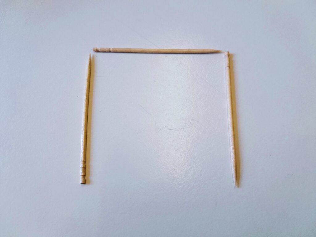 Photo of three toothpicks arranged around three sides of a square, with a gap at the bottom