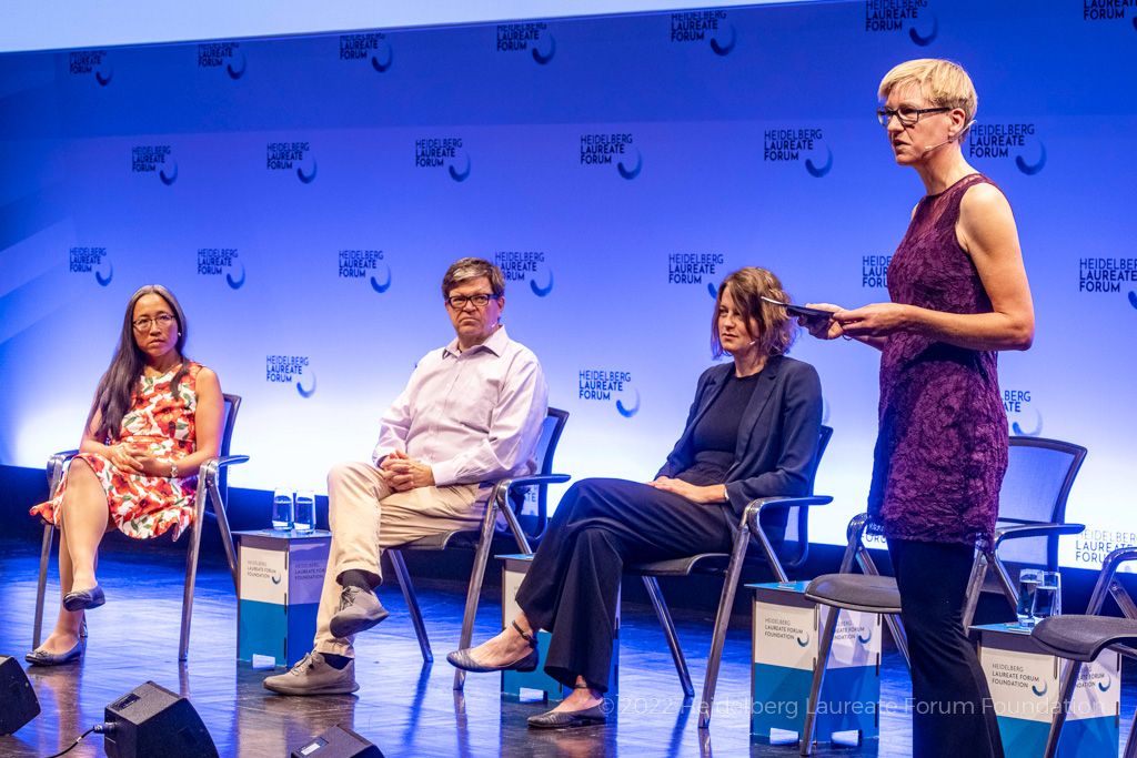A photograph of three of the panel on stage, including Yann LeCun, a middle-aged white man with short hair and glasses, wearing a light shirt; moderator Eva Wolfangel, a white woman with blonde hair in a dress, is standing on the right