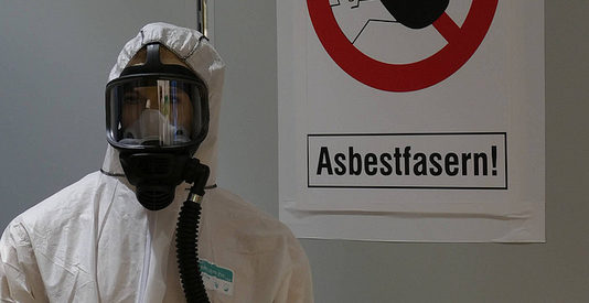 Warnschild "Achtung Asbest" und Person im Schutzanzug