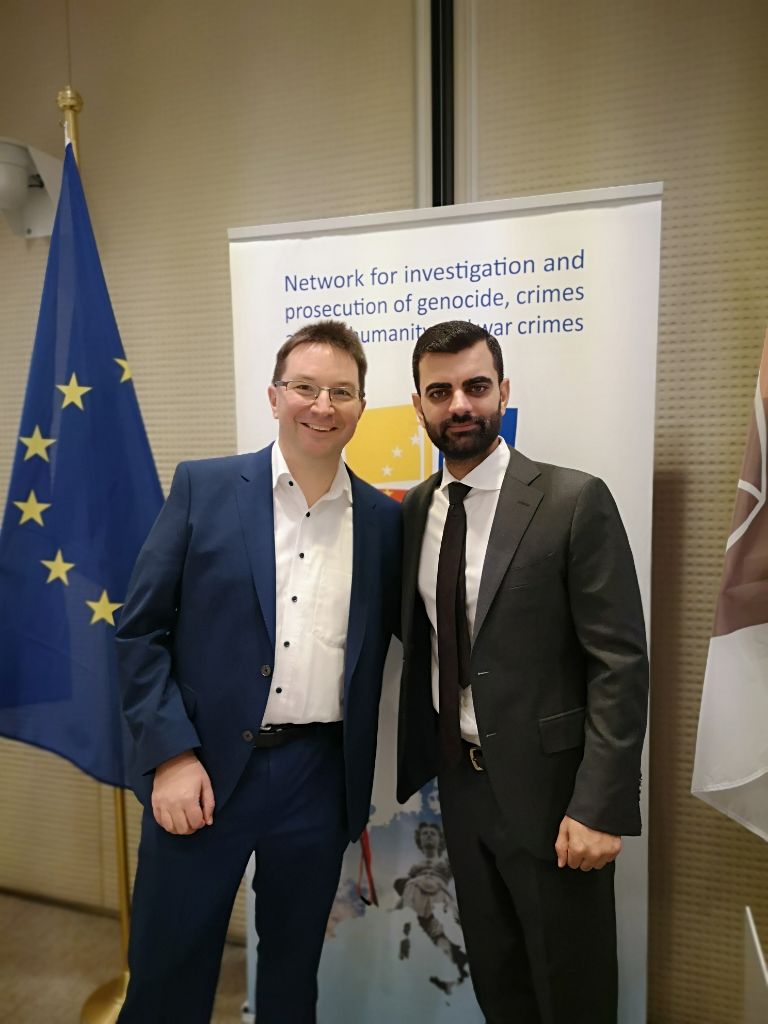 Dr. Michael Blume (left) and Abid Shamdeen (right) joining forces at the 34th Genocide Network conference by Eurojust, with a flag of the European Union behind them.