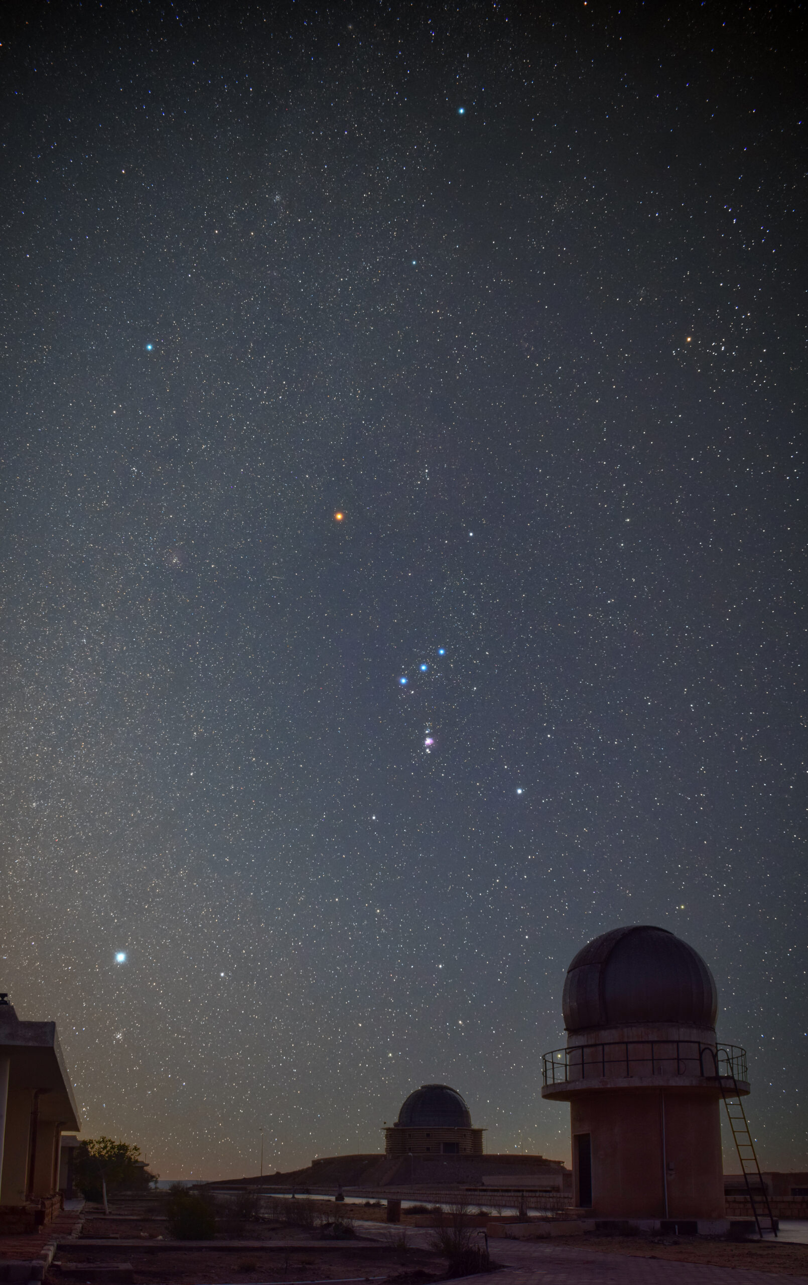 Orion mit Sternen in der Umgebung über einer Teleskopkuppel. Links oben am Orion haben wir mit Beteigeuze zwar nicht einen Roten Riesen, aber einen Roten Überriesen mit deutlicher orangener Färbung.